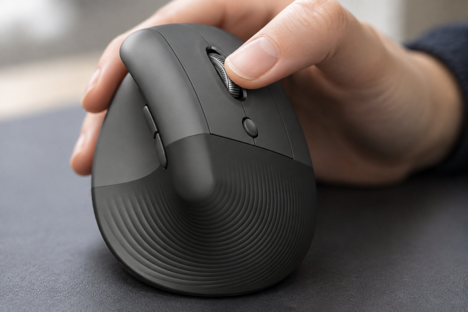 Une main tient une souris d’ordinateur noire posée sur une surface grise.
